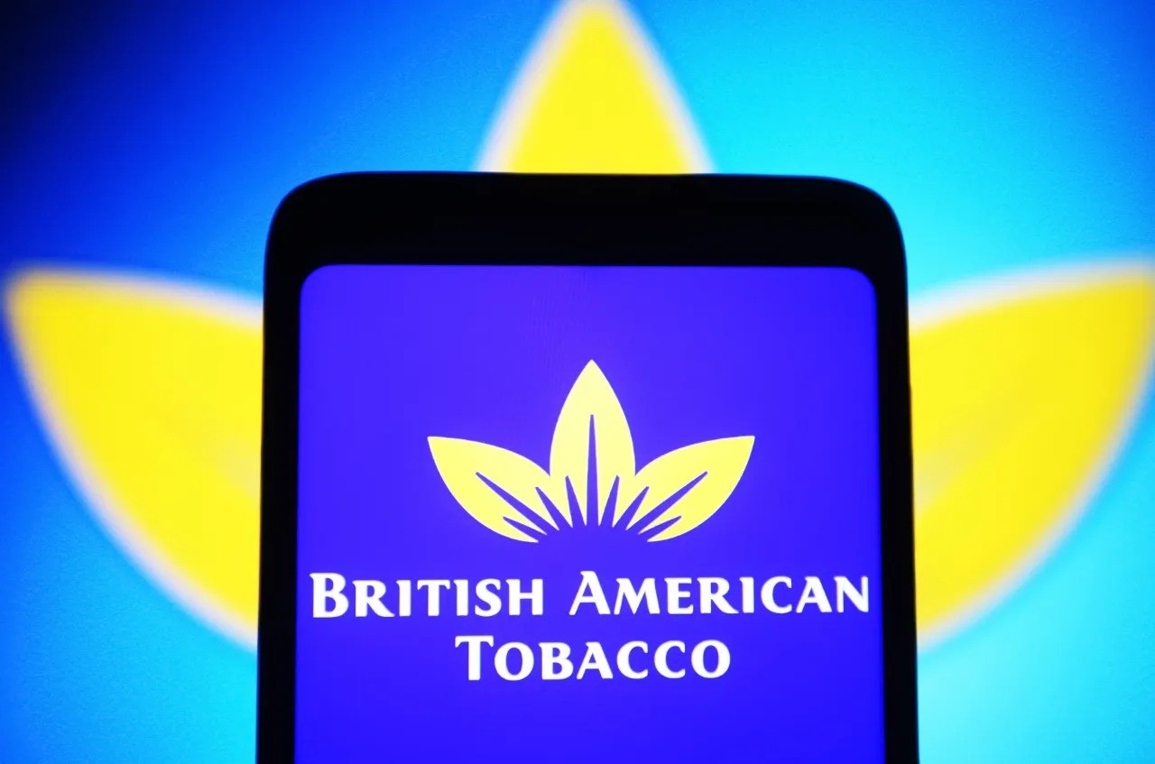 Smartphone shows British American Tobacco logo on purple screen with yellow-blue background. Smartphone shows British American Tobacco logo on purple screen with yellow-blue background.