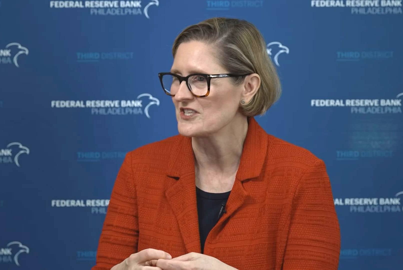 A woman speaks at the Federal Reserve Bank of Philadelphia's blue branded backdrop. A woman speaks at the Federal Reserve Bank of Philadelphia's blue branded backdrop.