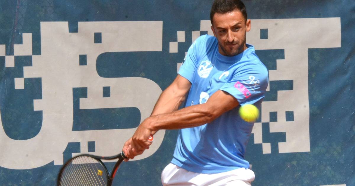 Male tennis player swings racket to hit yellow ball against blue banner backdrop. Male tennis player swings racket to hit yellow ball against blue banner backdrop.