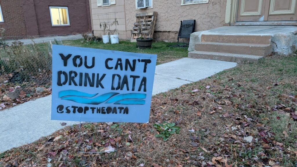A white Ford F-150 pickup displays "NO NO NO DATA CENTER" on its rear window in a suburban neighborhood. A white Ford F-150 pickup displays "NO NO NO DATA CENTER" on its rear window in a suburban neighborhood.