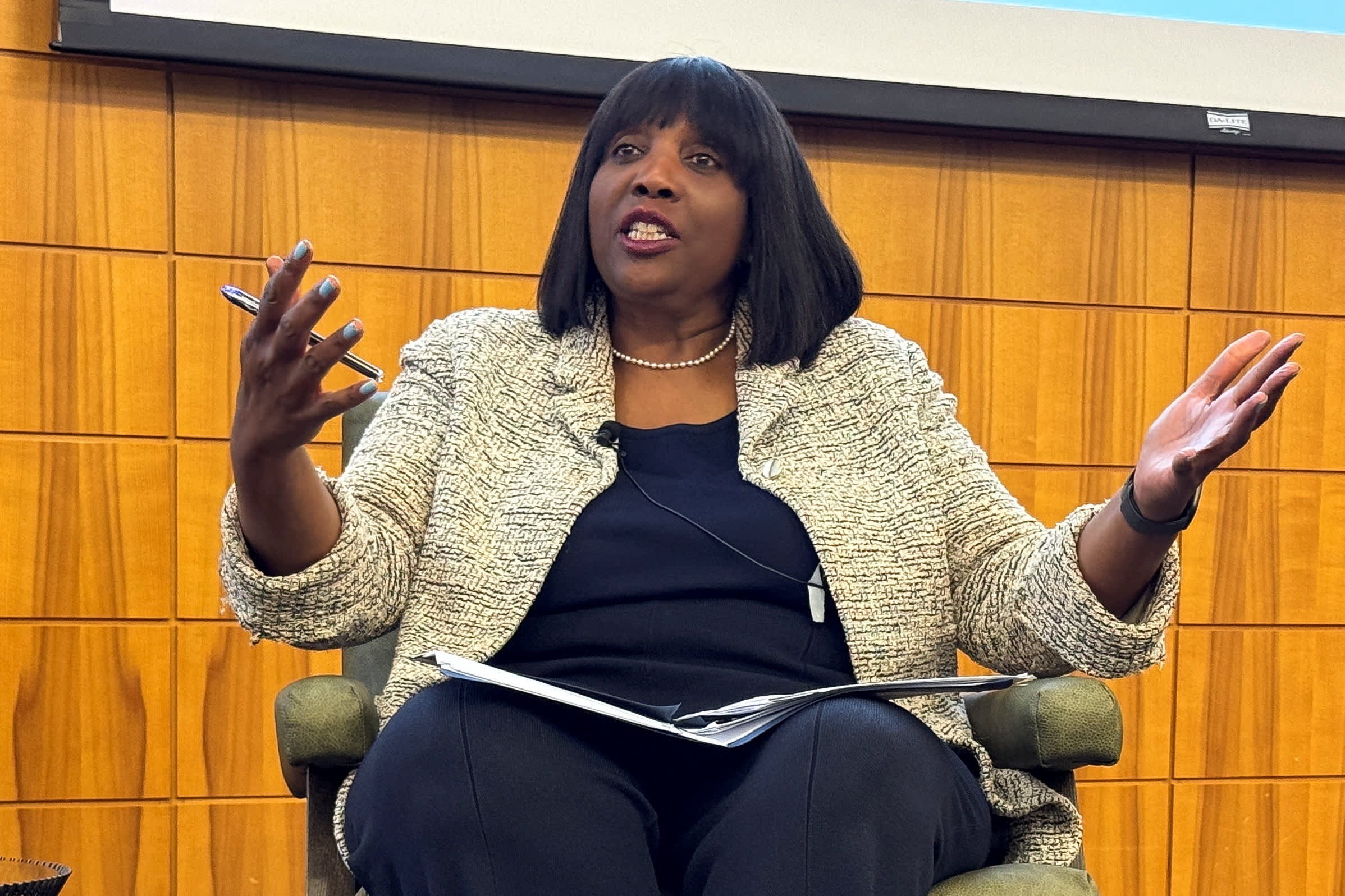 Woman gestures with hands while speaking indoors against a wooden panel wall. Woman gestures with hands while speaking indoors against a wooden panel wall.