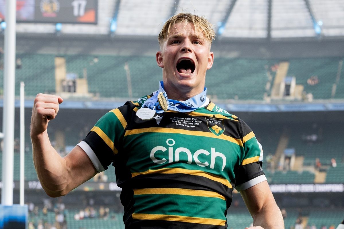 Rugby player wearing green-and-black jersey and medal celebrates with raised fist in stadium.