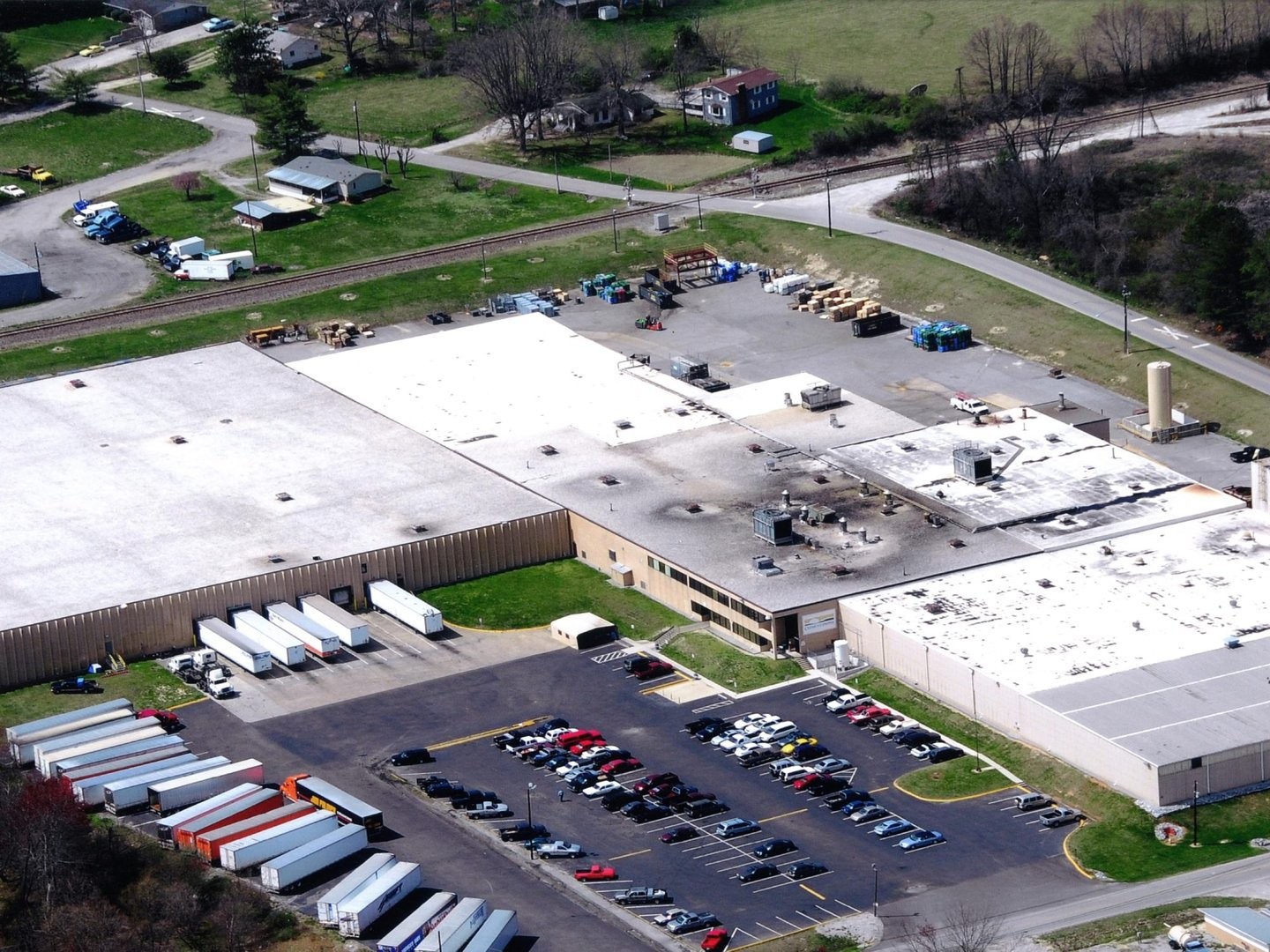 Aerial view of industrial complex in suburban area with warehouses, parking lots, and railroads.