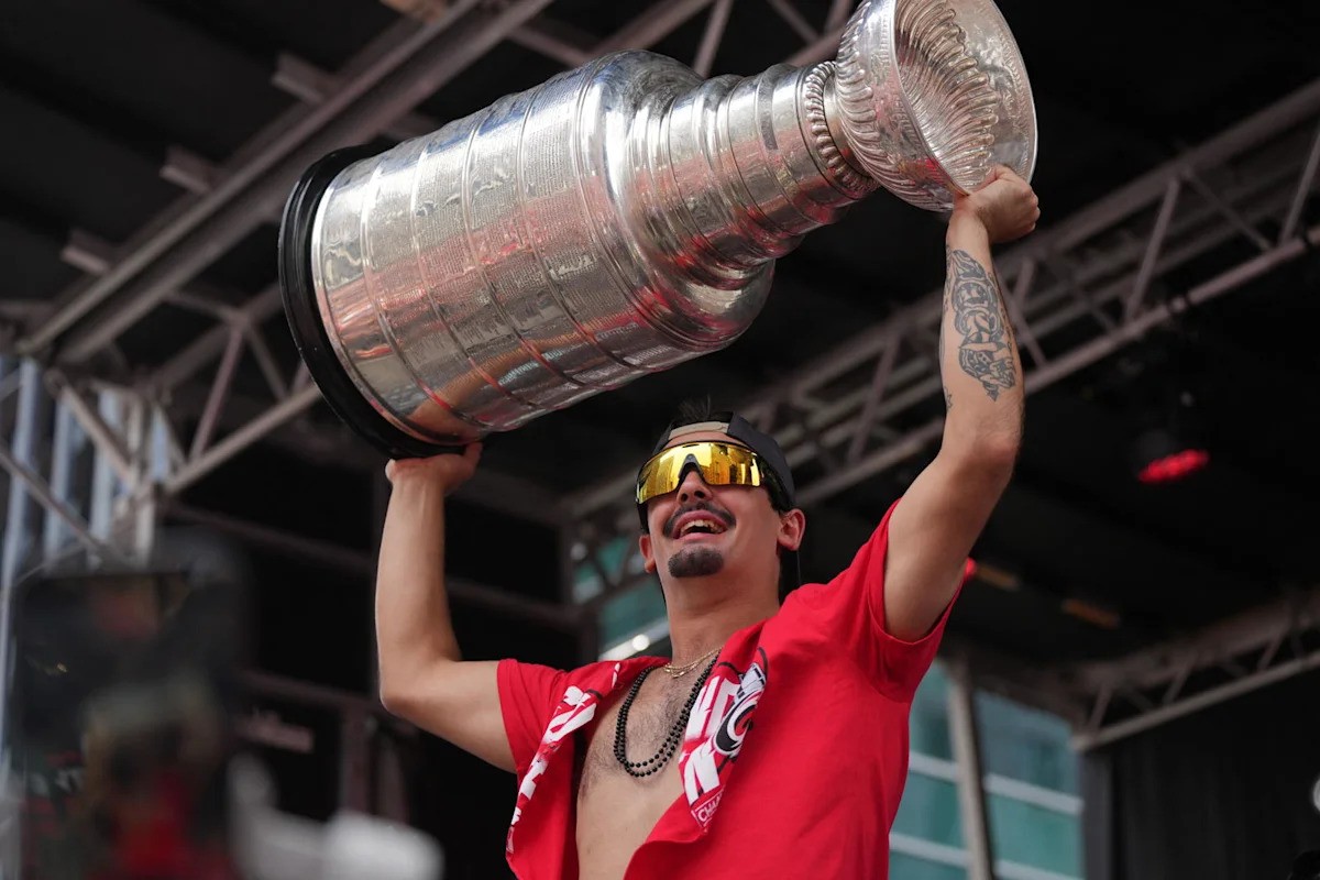 Man in red shirt lifts large silver trophy indoors at event venue.
