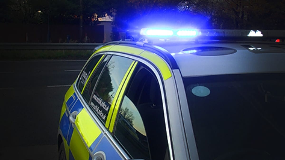 A police car with flashing blue lights is parked on a dark street at night. A police car with flashing blue lights is parked on a dark street at night.