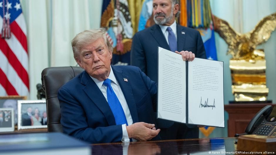 Donald Trump holds a signed document in the Oval Office. Donald Trump holds a signed document in the Oval Office.