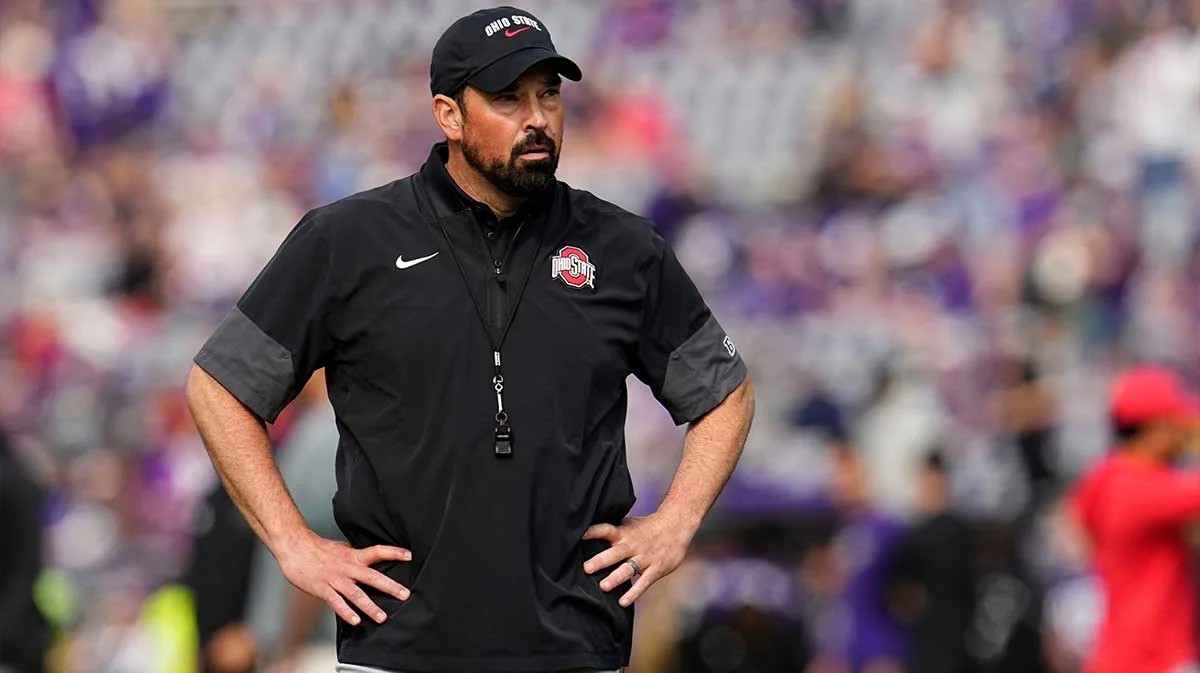 A man in an Ohio State cap and black polo stands with hands on hips at a crowded football stadium. A man in an Ohio State cap and black polo stands with hands on hips at a crowded football stadium.
