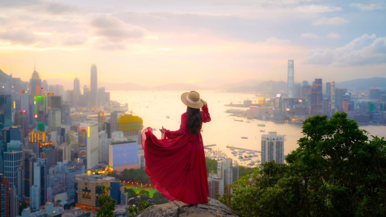 A woman in a red dress stands on a rock overlooking a city skyline at sunset. A woman in a red dress stands on a rock overlooking a city skyline at sunset.