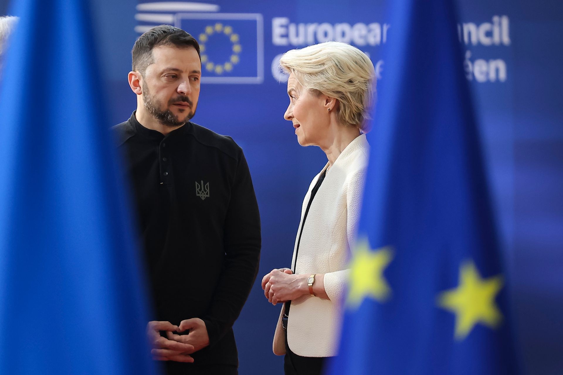 Two people converse at a European Council event with EU flags in background. Two people converse at a European Council event with EU flags in background.