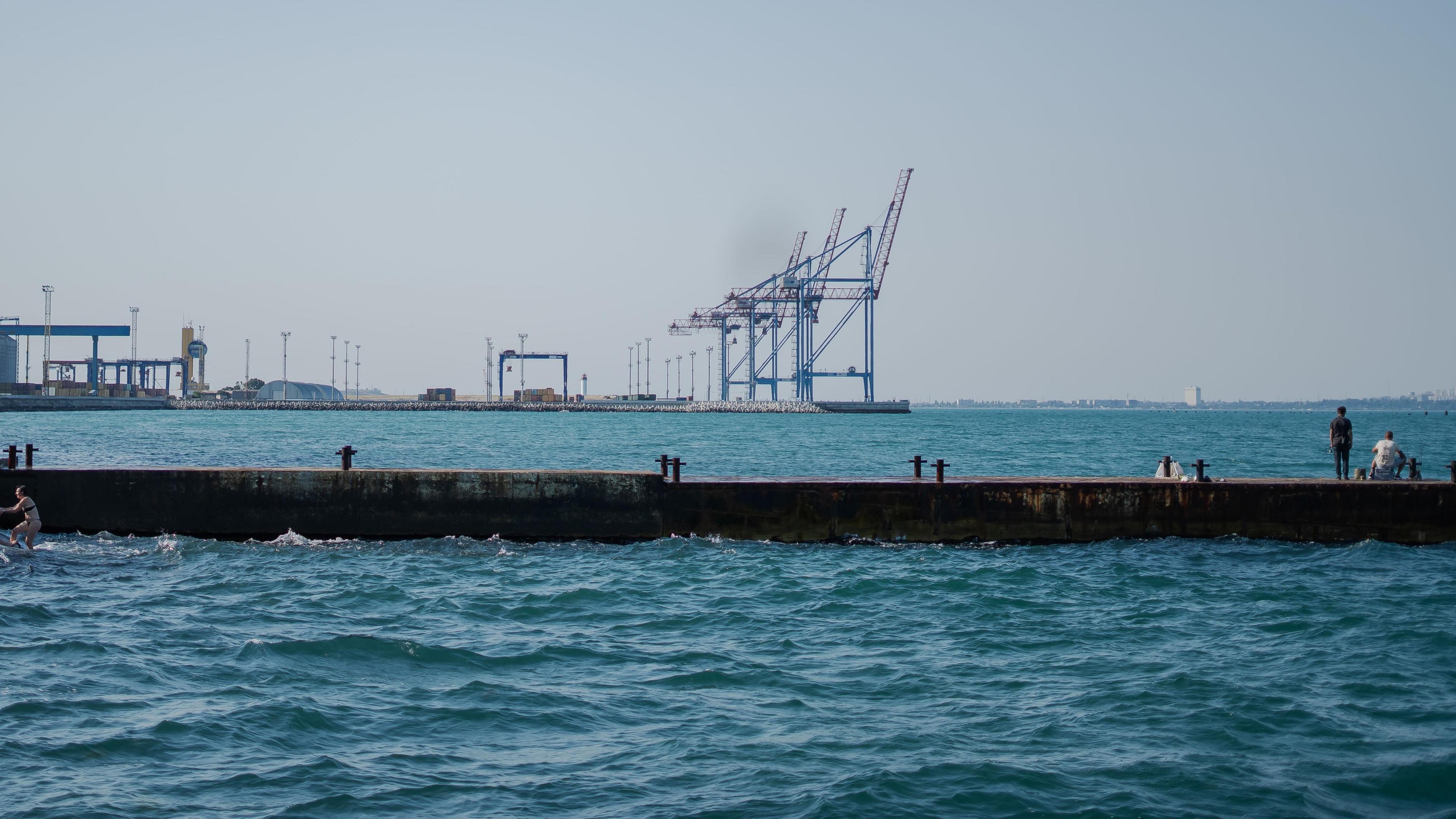 Fishermen on a concrete pier fish in the ocean with a distant ship visible. Fishermen on a concrete pier fish in the ocean with a distant ship visible.