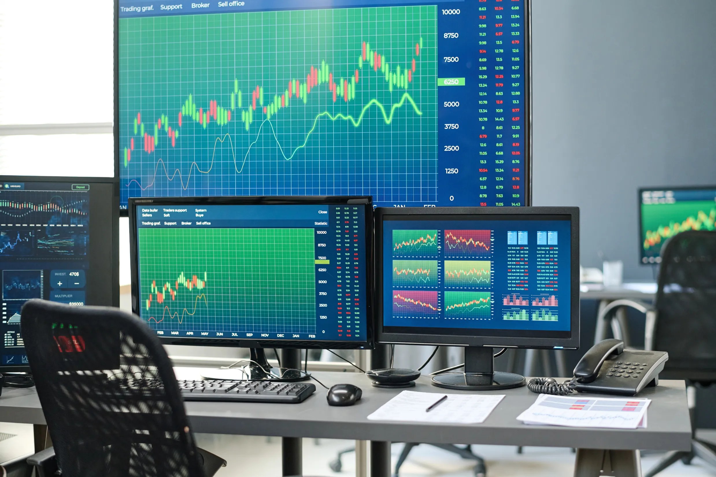 Trading workstation in office displays financial charts and market data on multiple monitors. Trading workstation in office displays financial charts and market data on multiple monitors.