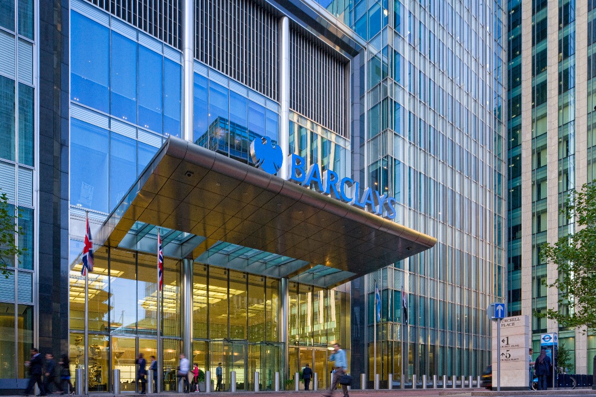 Barclays headquarters entrance with glass facade, UK flags, and pedestrians walking. Barclays headquarters entrance with glass facade, UK flags, and pedestrians walking.
