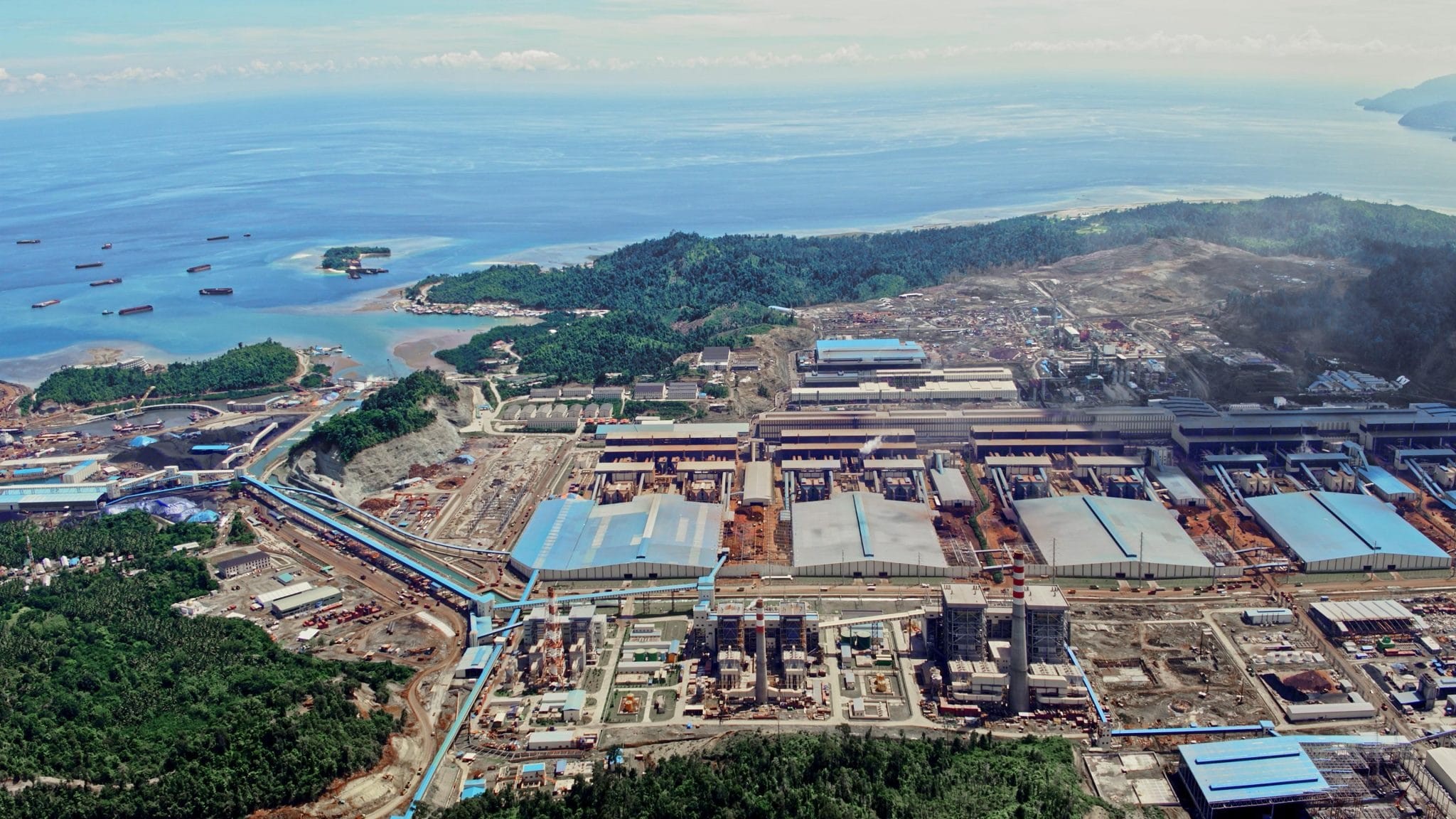 Aerial view of a large industrial complex on a coastal peninsula with ocean, ships, and construction activity. Aerial view of a large industrial complex on a coastal peninsula with ocean, ships, and construction activity.