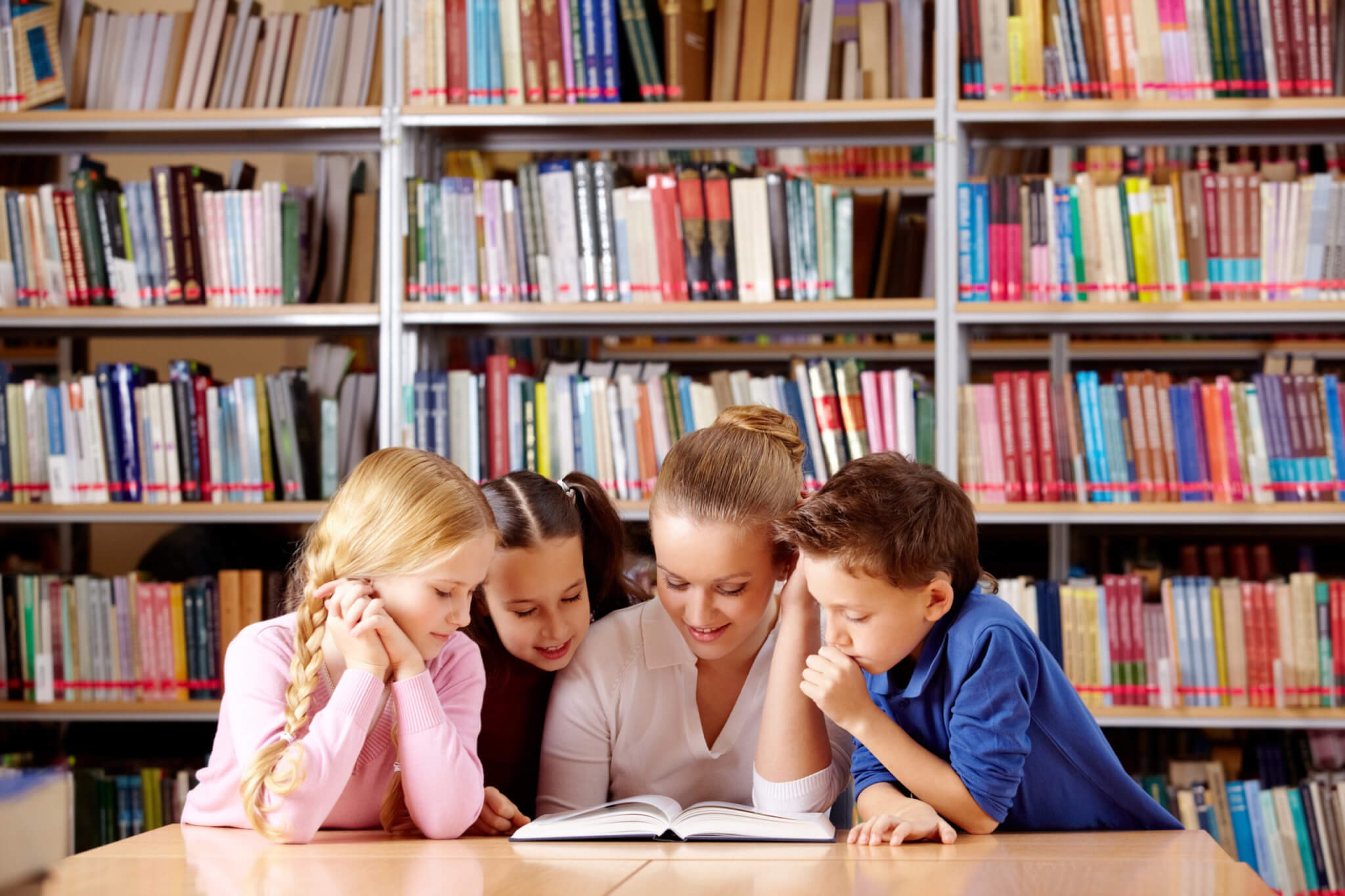 Four people read a book together at a table in a library. Four people read a book together at a table in a library.