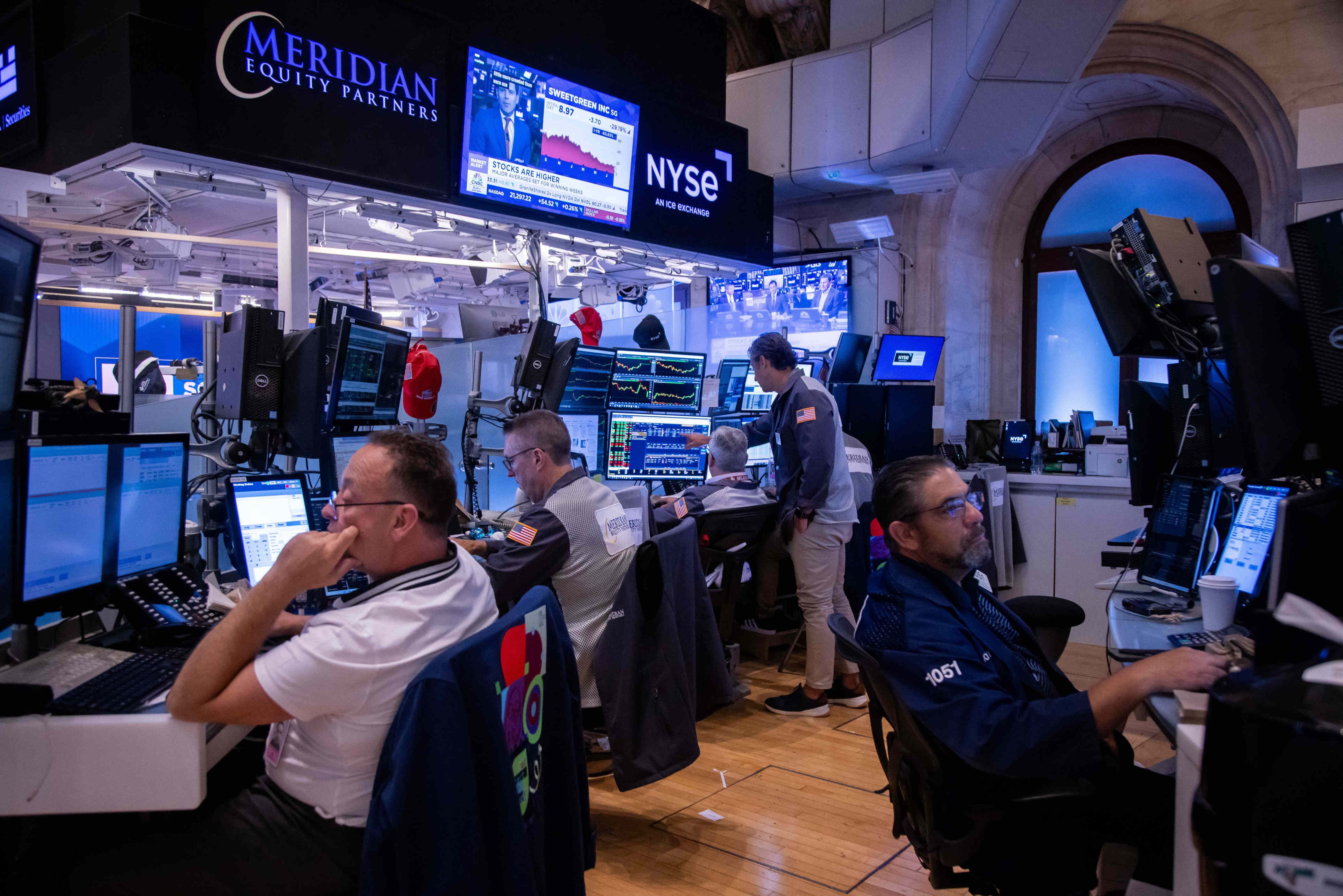 Traders work at desks with multiple monitors on an NYSE trading floor. Traders work at desks with multiple monitors on an NYSE trading floor.