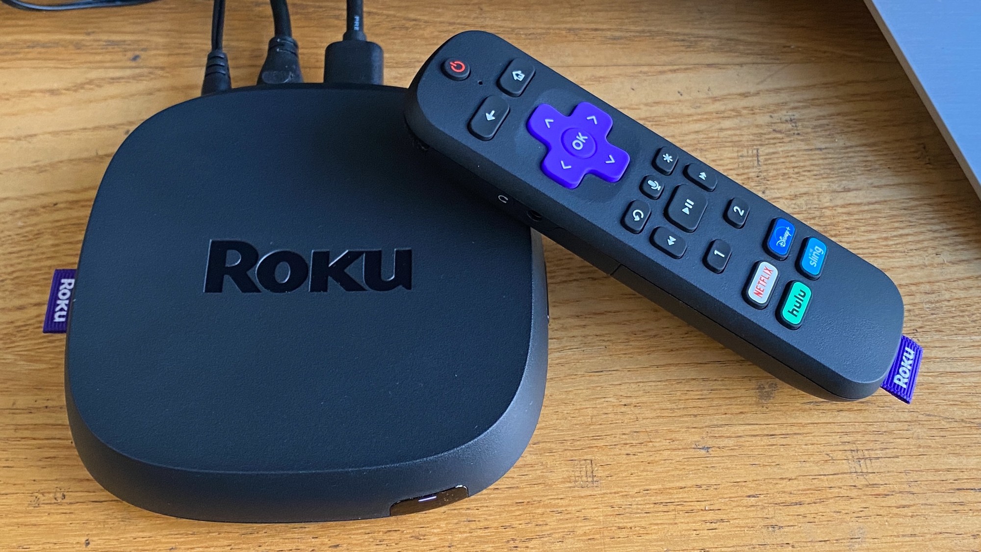Roku streaming device and remote lie on a wooden surface. Roku streaming device and remote lie on a wooden surface.