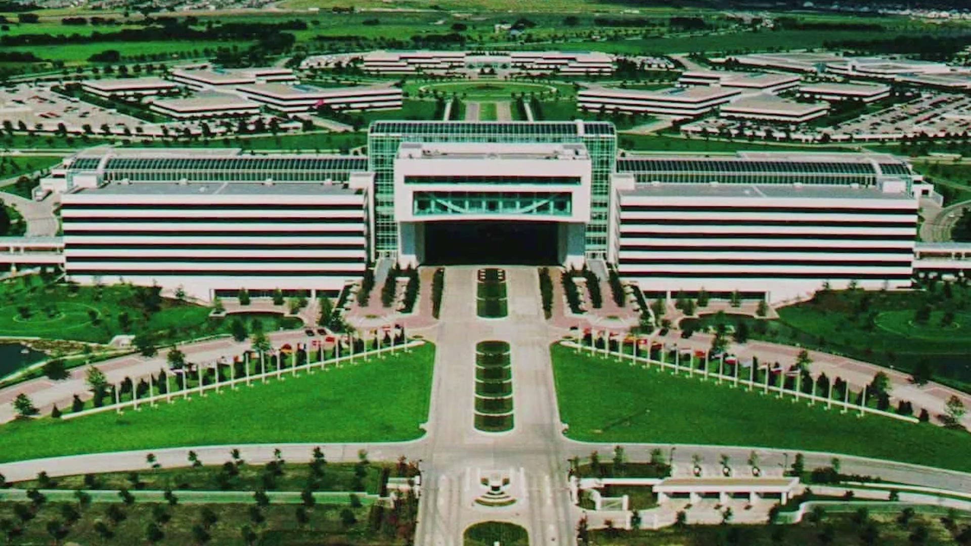 Aerial view of a large multi-building complex with central entrance, green lawns, and surrounding structures. Aerial view of a large multi-building complex with central entrance, green lawns, and surrounding structures.