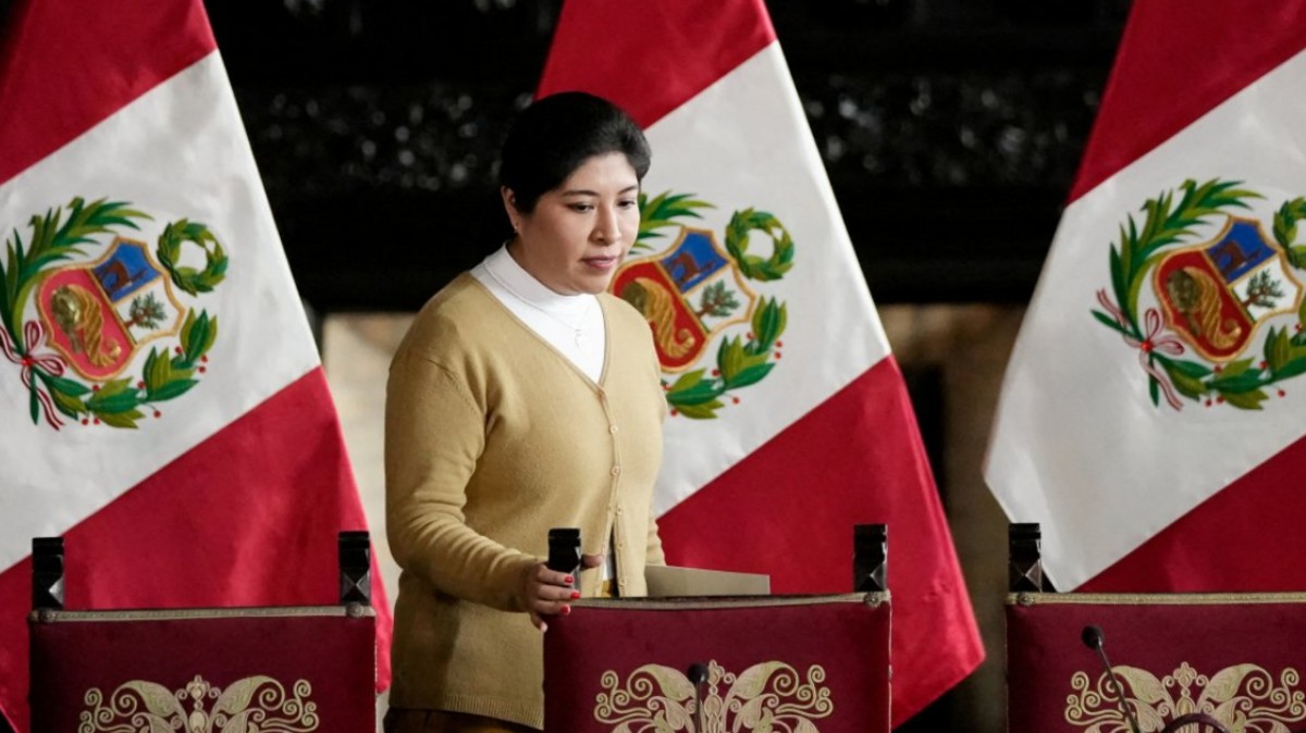 A woman speaks at a podium before Peruvian national flags.