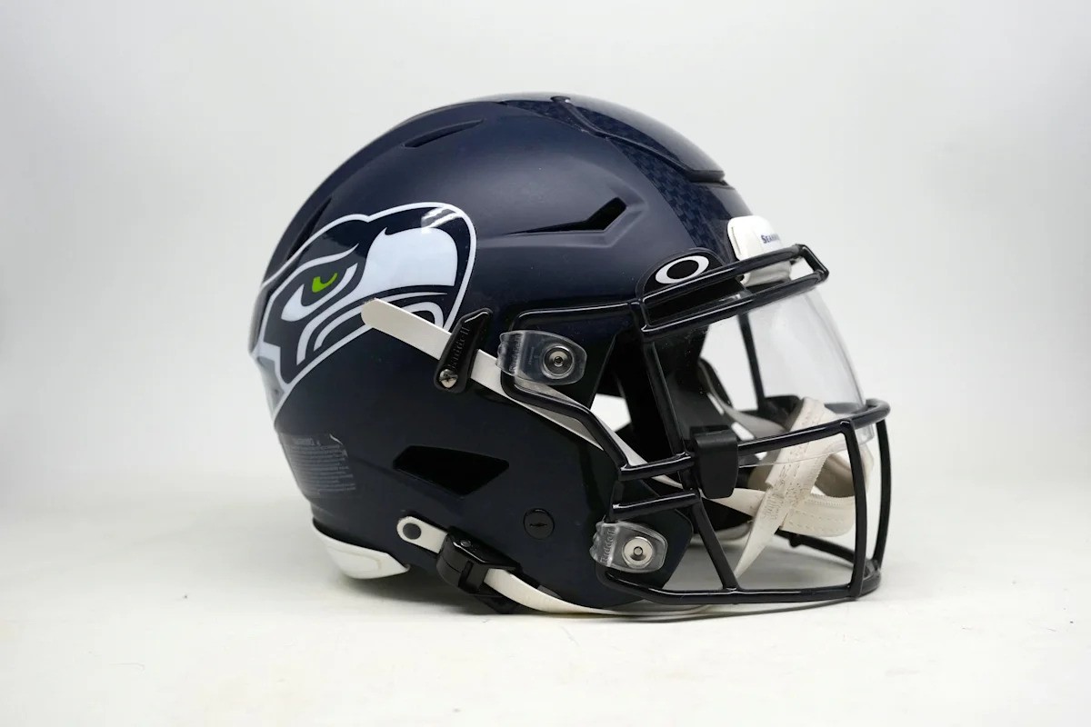 A dark blue Seattle Seahawks football helmet rests on a plain white surface. A dark blue Seattle Seahawks football helmet rests on a plain white surface.