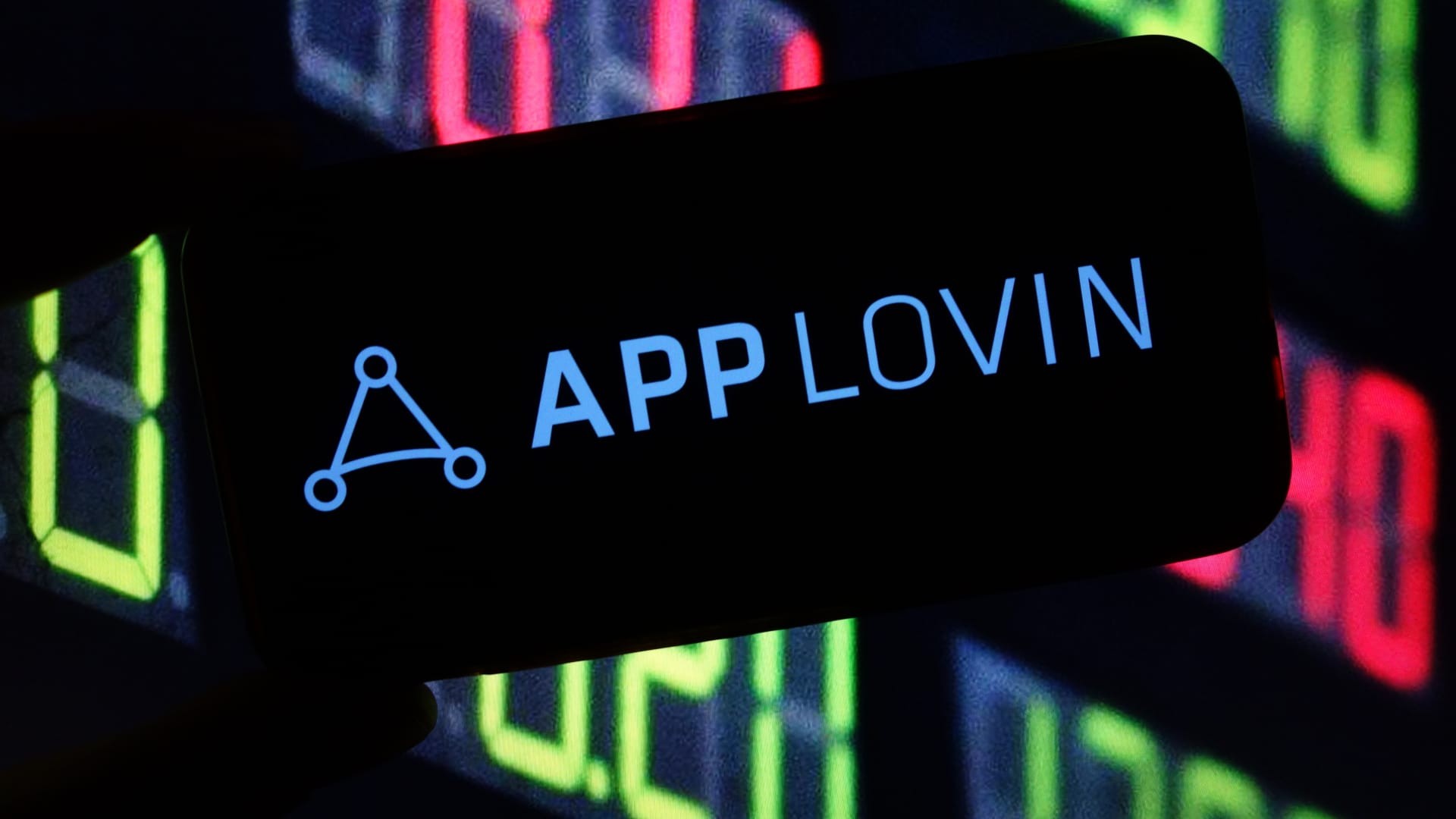 Smartphone screen displays "APPLLOVIN" logo against blurred stock market ticker background.