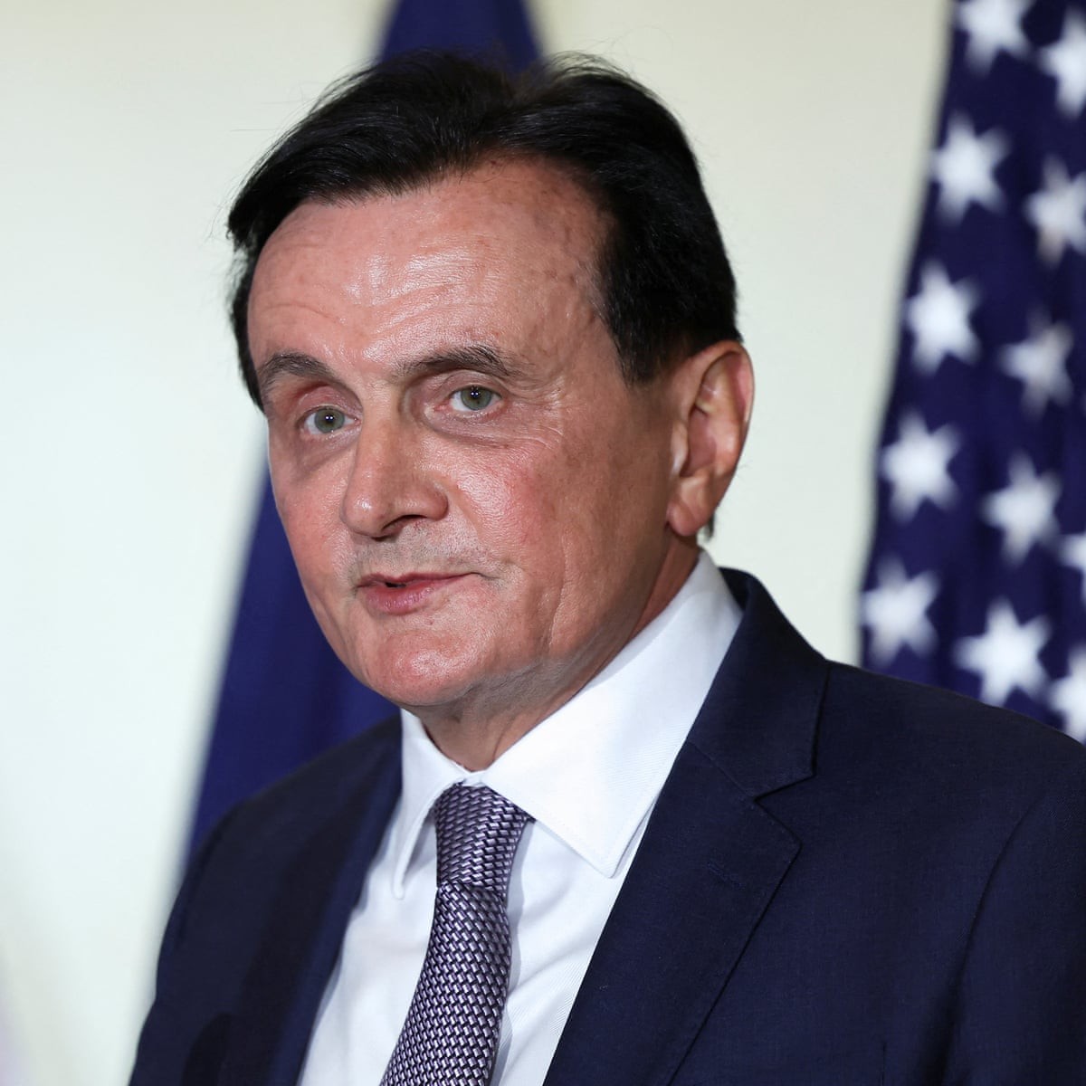 A man in a dark suit stands before Australian and American flags. A man in a dark suit stands before Australian and American flags.