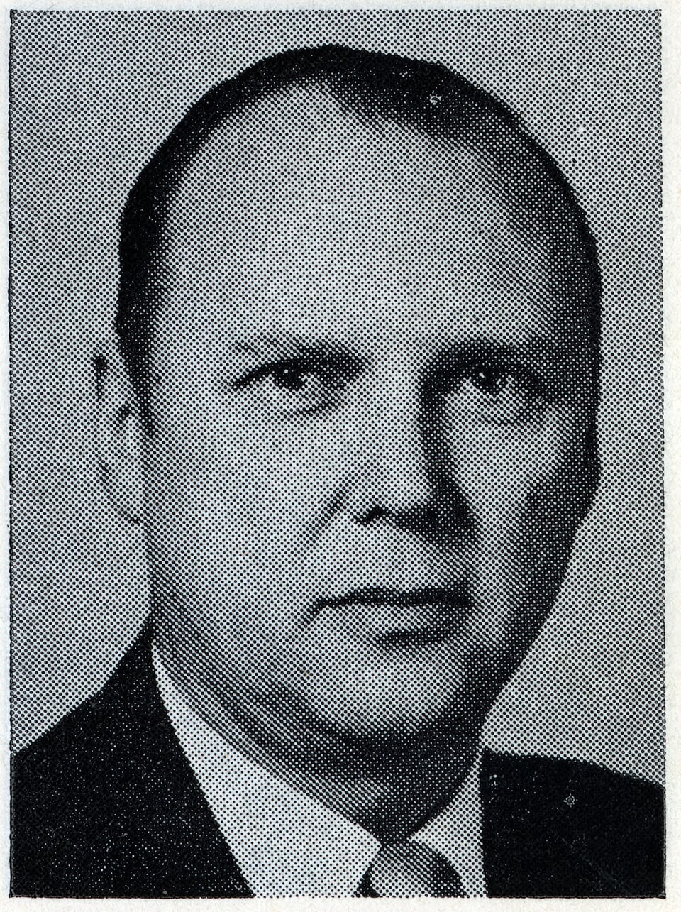 A man in a dark suit and tie poses for a black-and-white portrait photograph. A man in a dark suit and tie poses for a black-and-white portrait photograph.