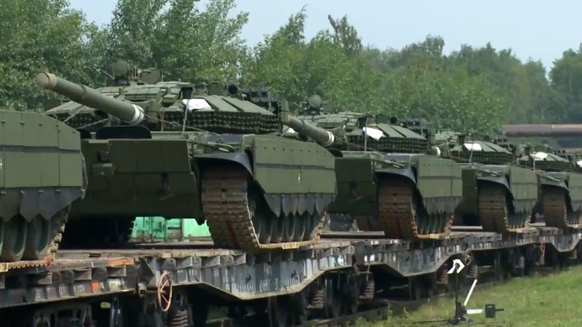Tanks are transported on flatbed railcars through a forested area. Tanks are transported on flatbed railcars through a forested area.