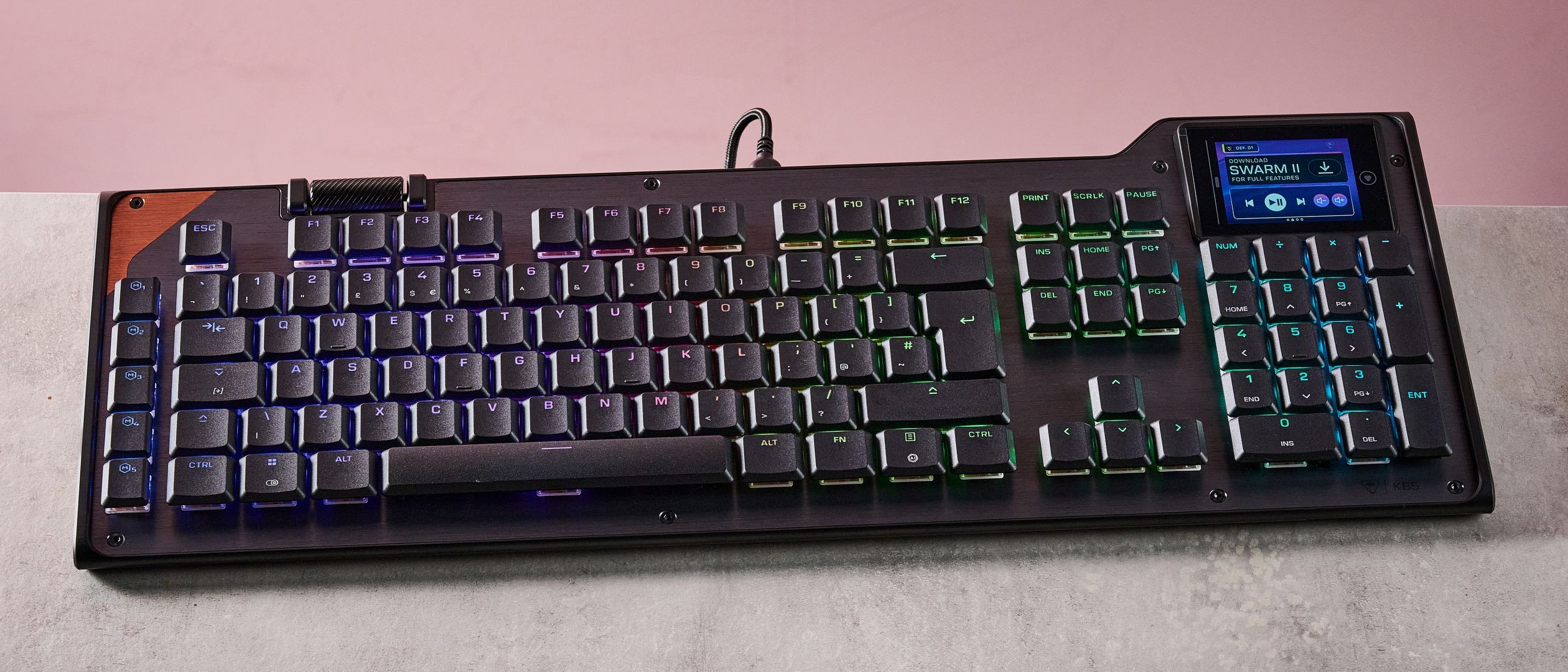 A backlit gaming keyboard rests on a concrete surface against a pink backdrop. A backlit gaming keyboard rests on a concrete surface against a pink backdrop.