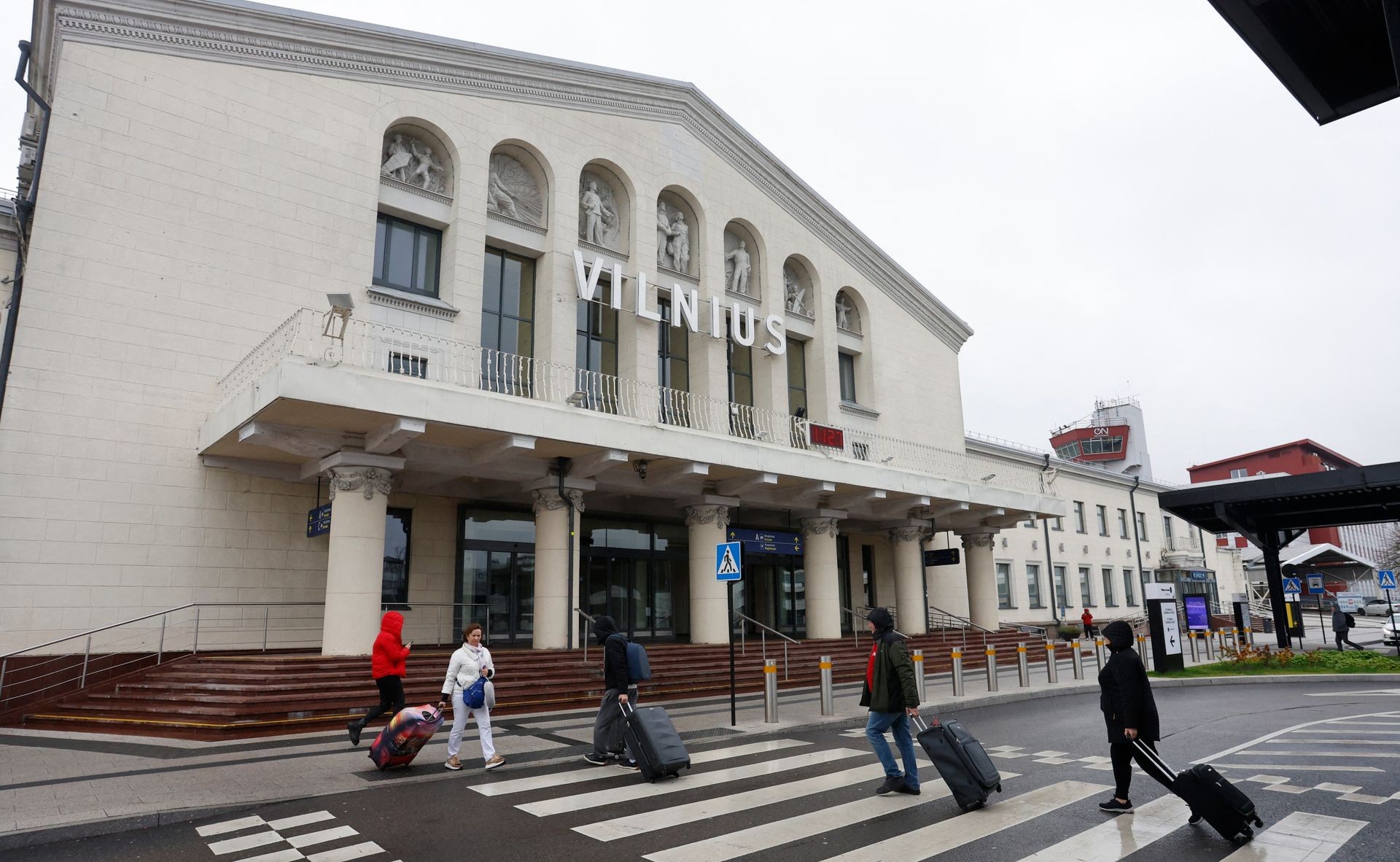 Pedestrians with rolling suitcases cross a zebra crossing in front of the Vilnius building. Pedestrians with rolling suitcases cross a zebra crossing in front of the Vilnius building.