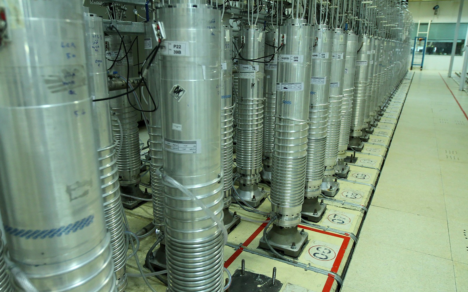 Rows of labeled metallic cylinders stand in an indoor technical facility on marked floor tiles.