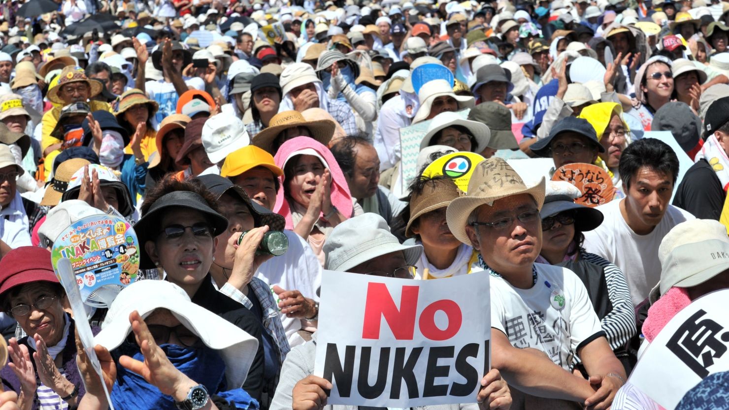 A crowd of protesters holds "No Nukes" signs at an outdoor demonstration. A crowd of protesters holds "No Nukes" signs at an outdoor demonstration.
