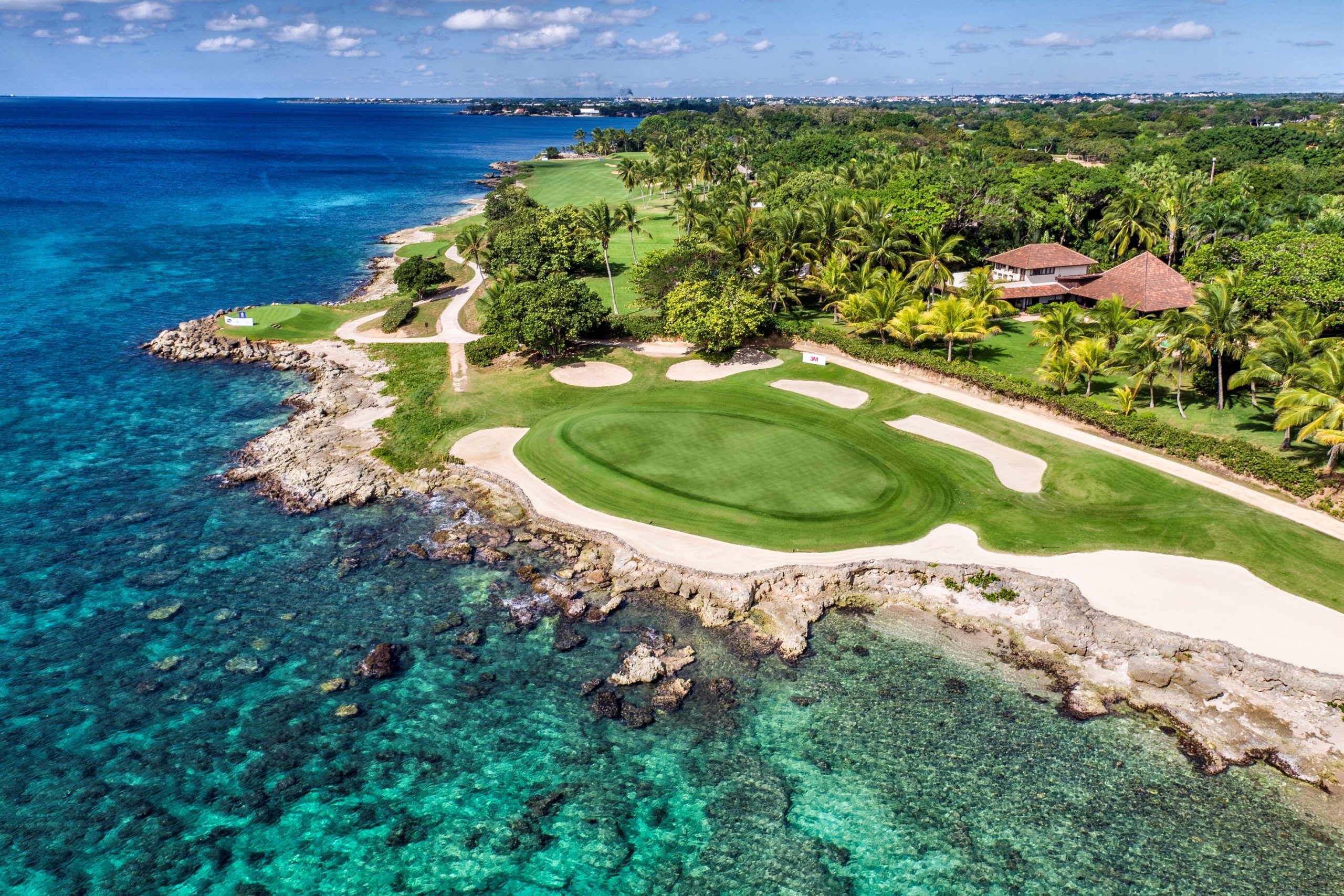 Coastal golf course features green fairways, sand traps, and buildings along turquoise ocean waters. Coastal golf course features green fairways, sand traps, and buildings along turquoise ocean waters.