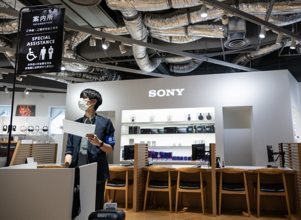 Masked staff member holds paper at Sony store information counter. Masked staff member holds paper at Sony store information counter.