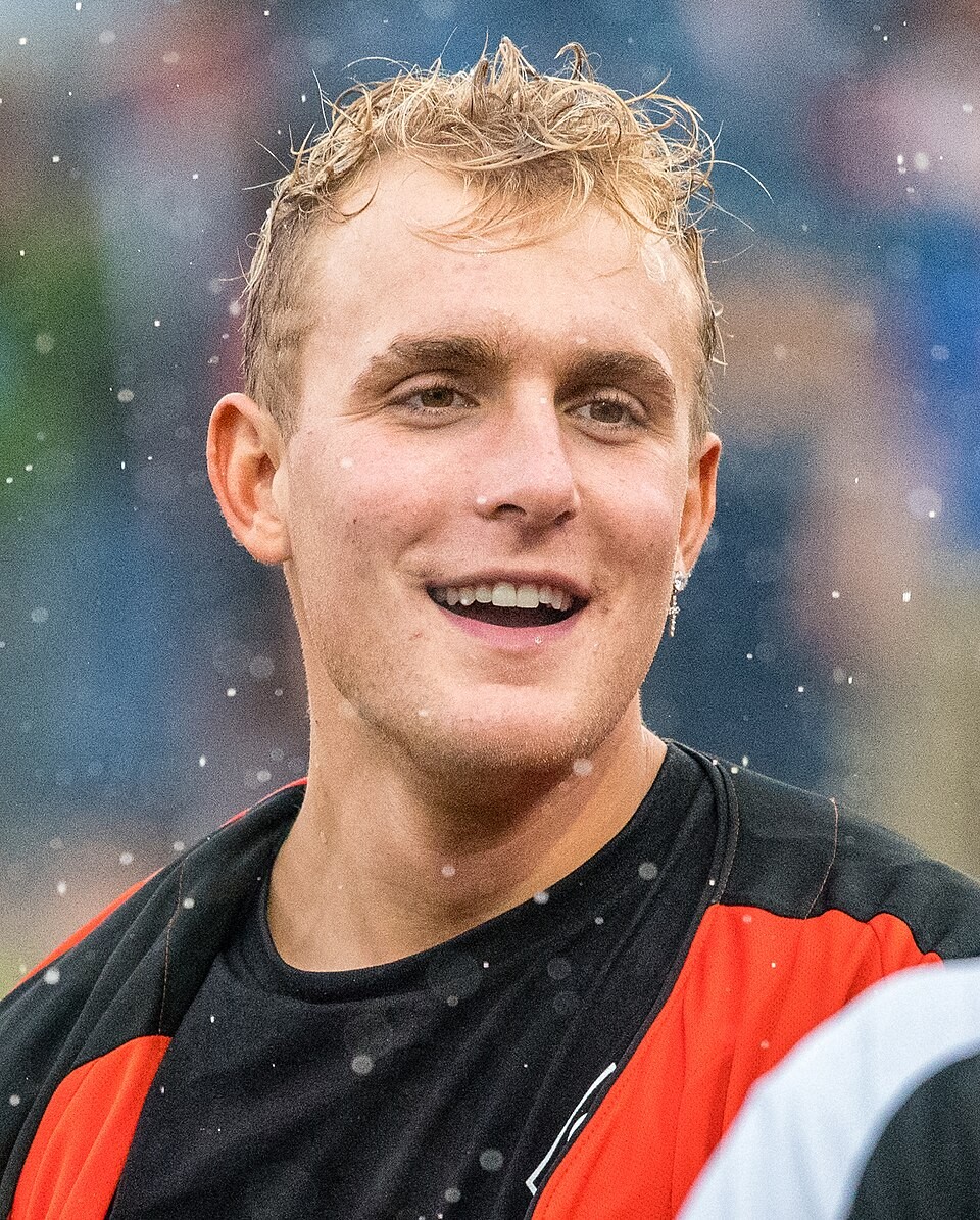 A man with wet hair wears a black-and-red sports top, smiling amid snow at a stadium.