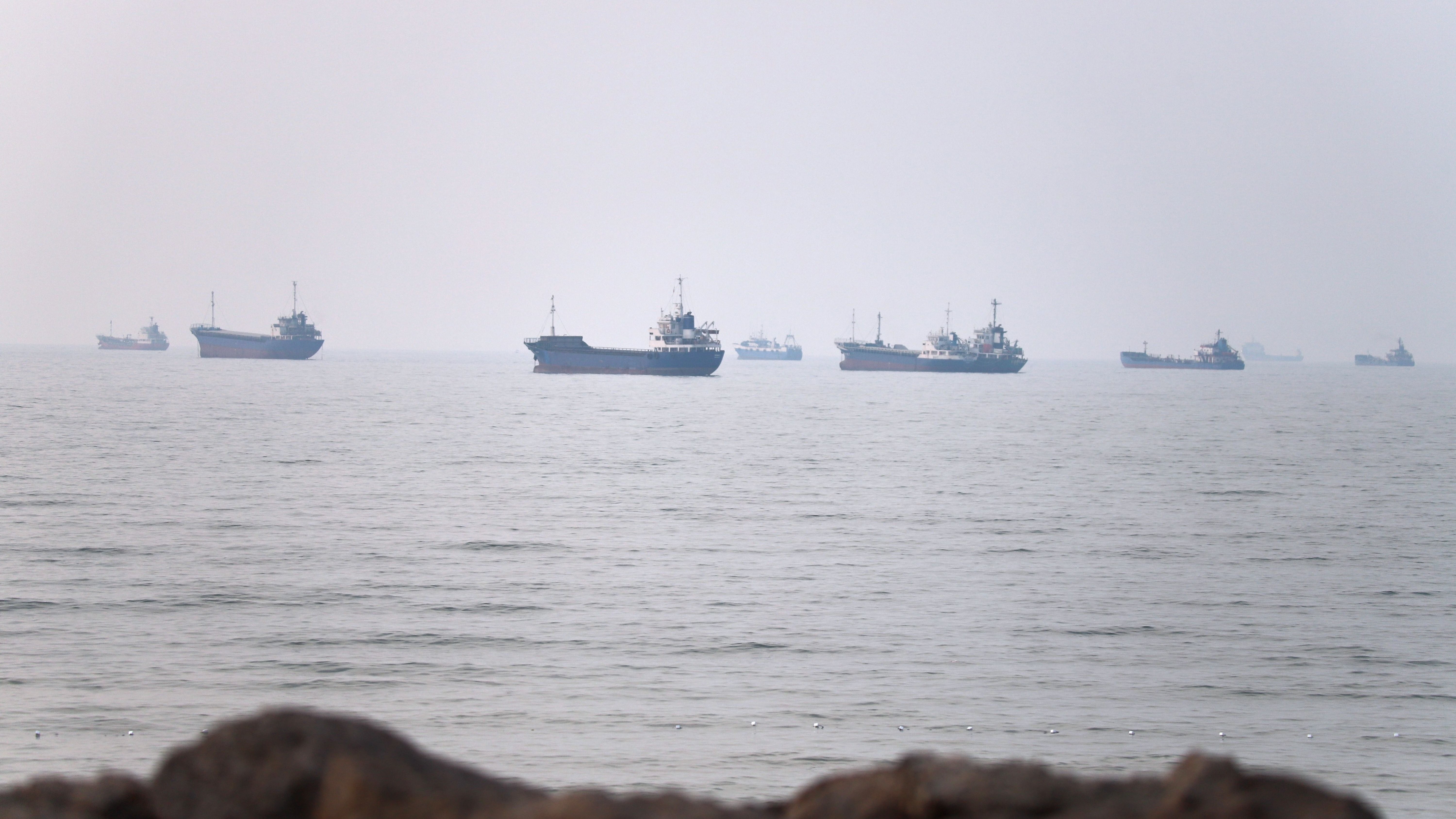 Multiple ships float on a calm ocean under an overcast sky. Multiple ships float on a calm ocean under an overcast sky.