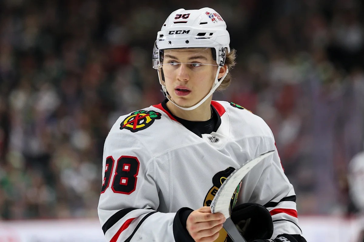 Hockey player wearing #98 jersey holds stick on ice rink during game. Hockey player wearing #98 jersey holds stick on ice rink during game.