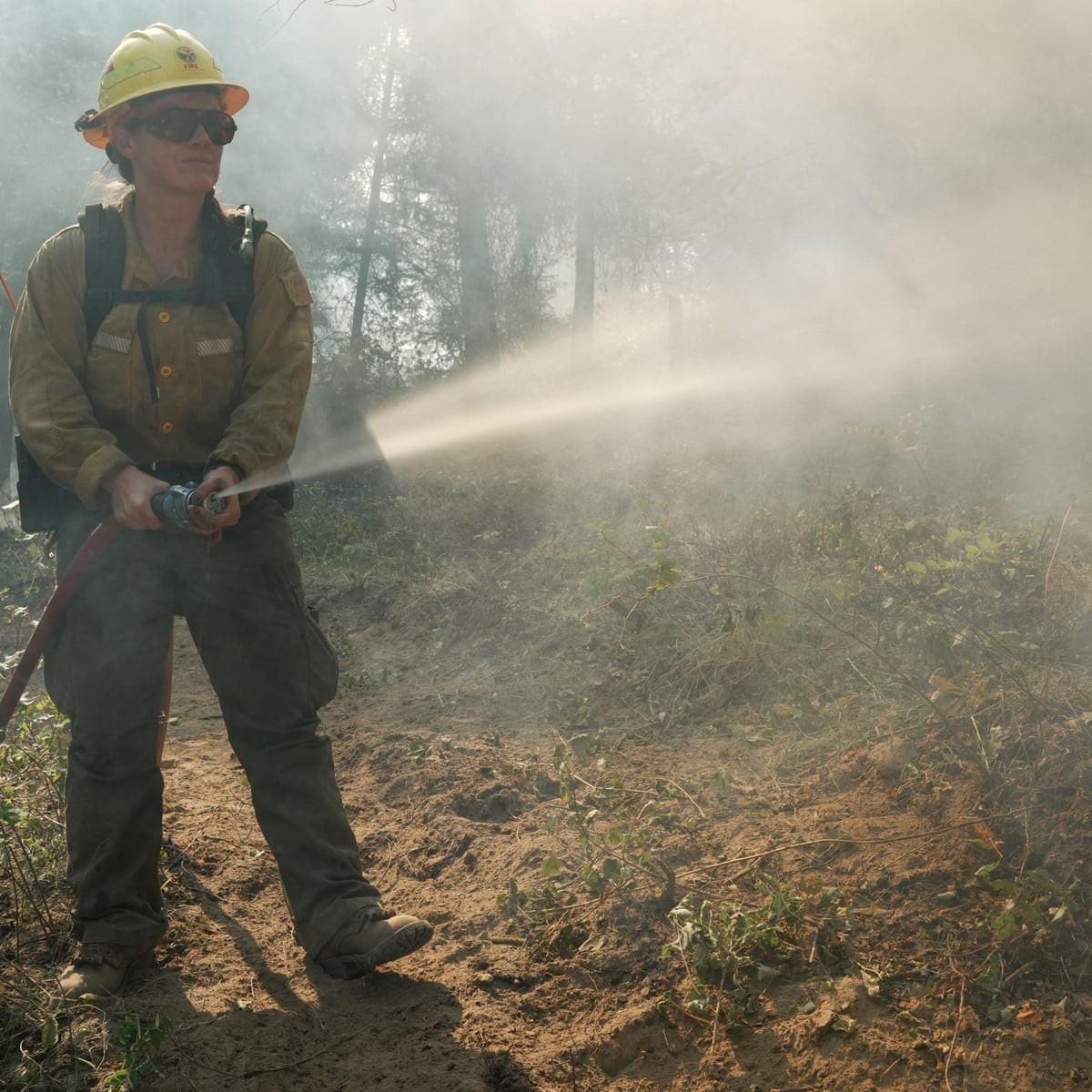 A firefighter sprays water from a hose in a smoky forested area. A firefighter sprays water from a hose in a smoky forested area.