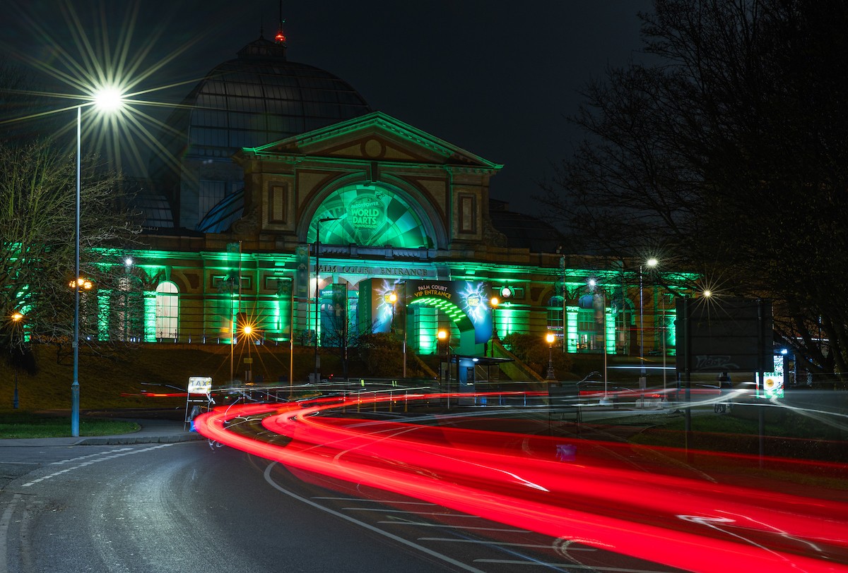 Nighttime photo of a green-lit building with red car light trails on an urban road. Nighttime photo of a green-lit building with red car light trails on an urban road.