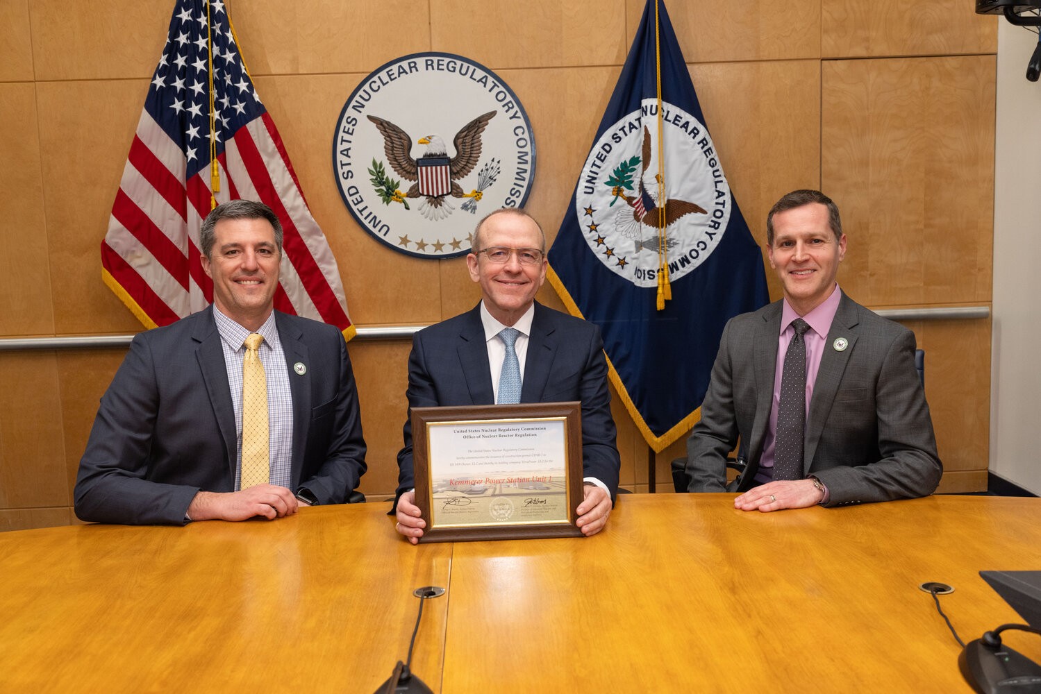 Three men pose at a U.S. Nuclear Regulatory Commission table with a framed award. Three men pose at a U.S. Nuclear Regulatory Commission table with a framed award.