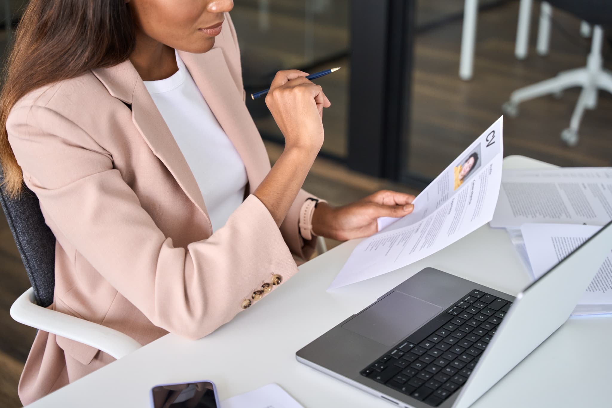 Office worker holds resume and pen at desk with laptop nearby. Office worker holds resume and pen at desk with laptop nearby.