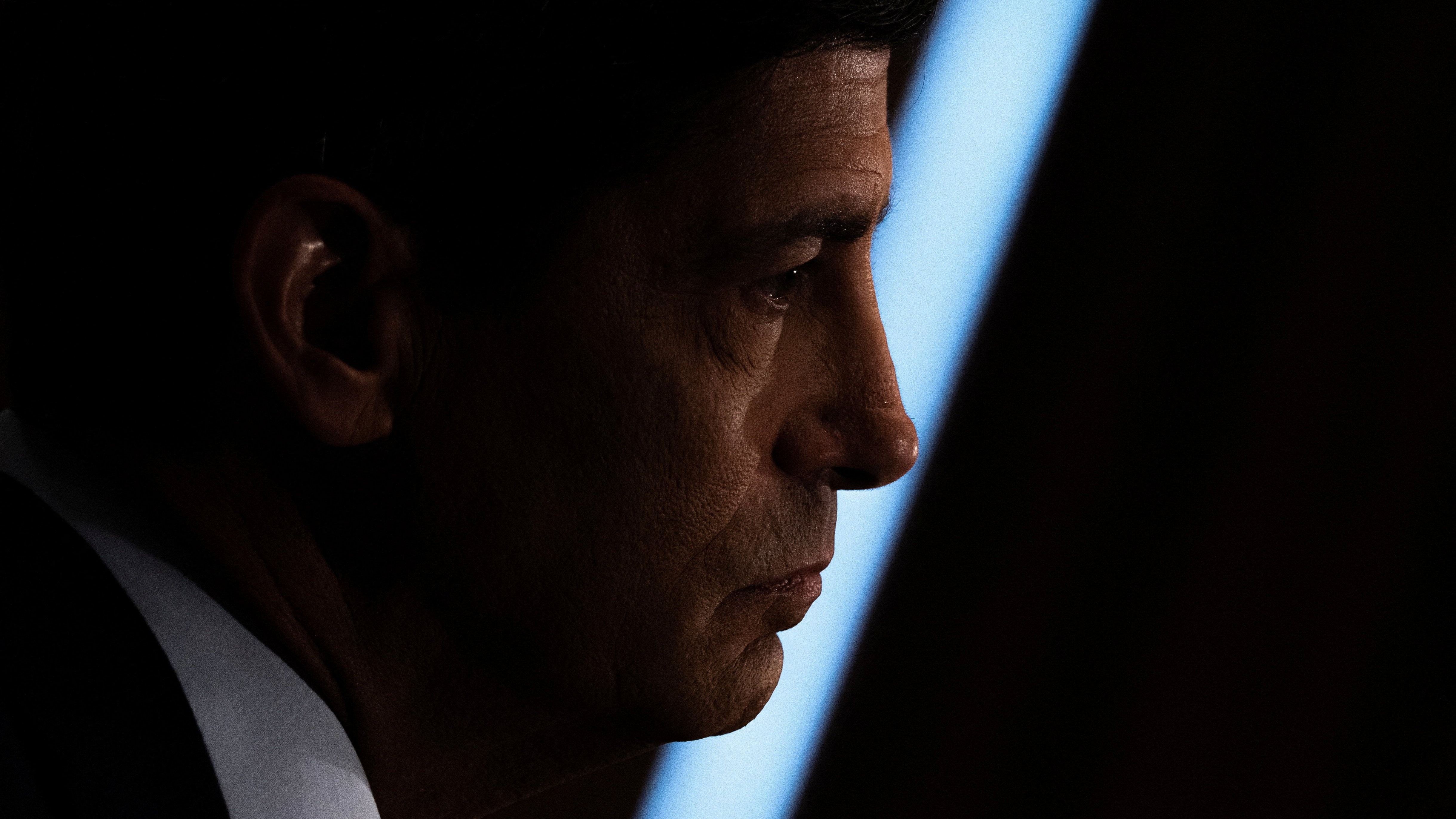 Man in suit profile looks toward dark object against blue-lit background. Man in suit profile looks toward dark object against blue-lit background.