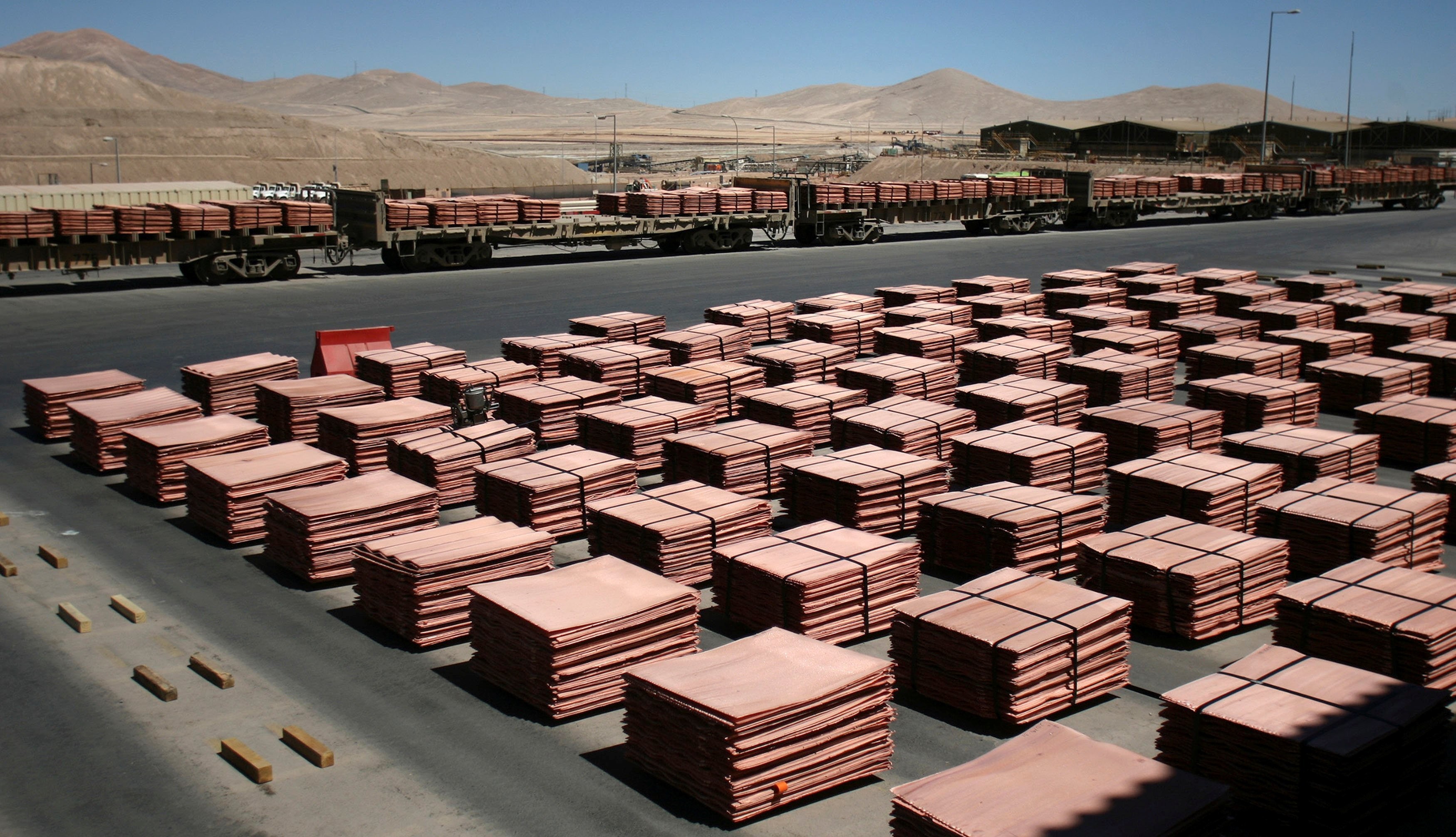 Copper sheets are stacked on an industrial yard with railcars loaded nearby. Copper sheets are stacked on an industrial yard with railcars loaded nearby.